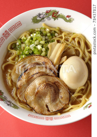 A bird's-eye view of pork bone soy sauce ramen containing roasted char siu, taste balls, menma and all-purpose green onions on a red background 78437817