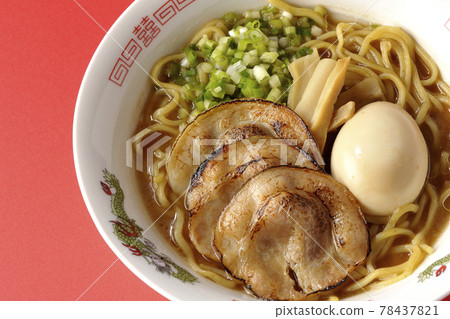 A bird's-eye view of pork bone soy sauce ramen containing roasted char siu, taste balls, menma and all-purpose green onions on a red background 78437821