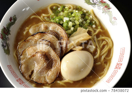 A bird's-eye view of pork bone soy sauce ramen containing roasted char siu, taste balls, menma and all-purpose green onions on a black background 78438072