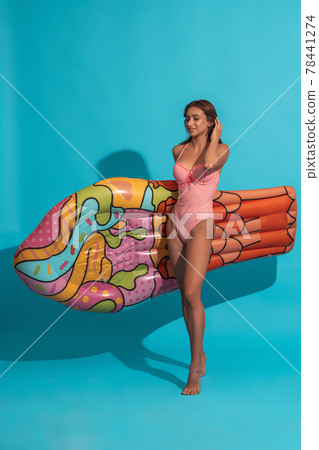 Smiling girl in swimsuit carrying inflatable mattress on blue background Smiling girl in swimsuit carrying inflatable mattress on blue background 78441274