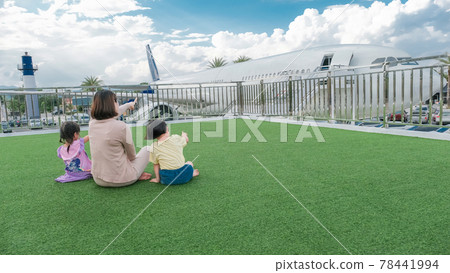 The back view of happy family mother woman and baby kids, pointing fun to the plane 78441994