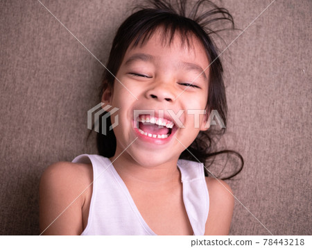 Cute little girl lying on sofa in the living room, looking at camera and smiling while playing at home. Cute little girl lying on sofa in the living room, looking at camera and smiling while playing at home. 78443218
