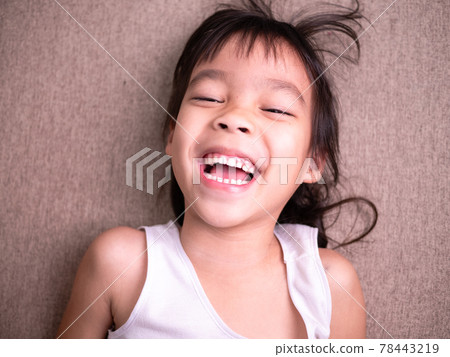 Cute little girl lying on sofa in the living room, looking at camera and smiling while playing at home. Cute little girl lying on sofa in the living room, looking at camera and smiling while playing at home. 78443219