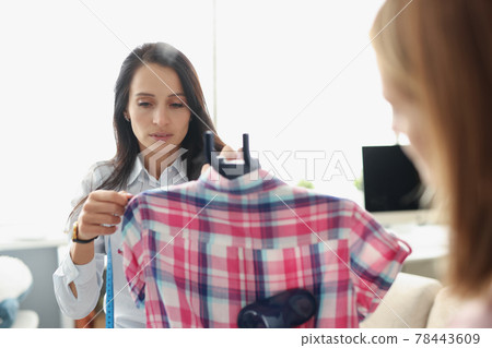 Women seamstresses taking measurements of shirts with centimeter tape and ironing with steamer 78443609