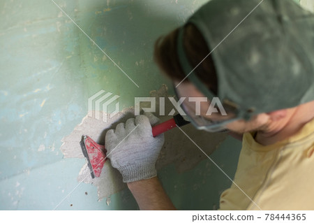 Caucasian man removing old paint with scraper tool. 78444365