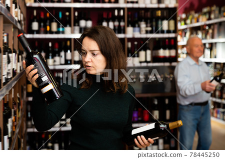 Focused woman customer buying bottle of wine Focused woman customer buying bottle of wine 78445250