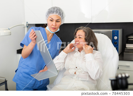 Professional cosmetologist examining female client face before procedure in esthetic clinic Professional cosmetologist examining female client face before procedure in esthetic clinic 78445303