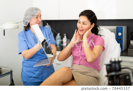 Portrait of a satisfied young female patient after the procedure, looking in the mirror 78445337