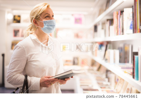 Mature woman in face mask looking at souvenir products Mature woman in face mask looking at souvenir products 78445661