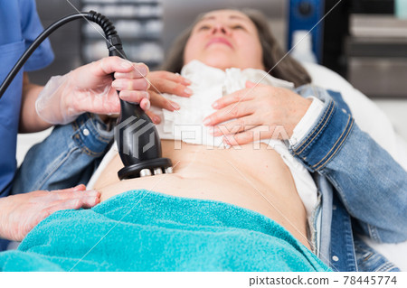 Young cosmetology doctor gives an elderly female client a vacuum abdominal massage Young cosmetology doctor gives an elderly female client a vacuum abdominal massage 78445774