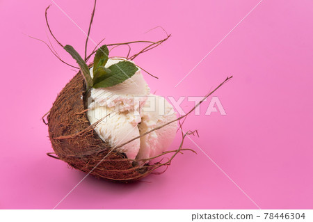 Vanilla ice cream balls in an empty coconut decorated with mint leaves on a pink background 78446304
