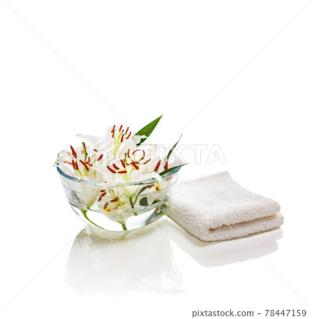 Transparent vase with water and white lilies with a white towel. Isolated on white. Spa concept for cleanliness, freshness and aromatherapy. 78447159
