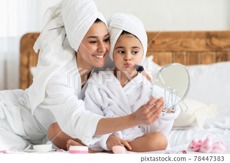 Pretty mother applying blush on her kid cheek Pretty mother applying blush on her kid cheek 78447383