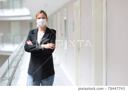 Businesswoman in medical protective mask stands with folded arms in hotel corridor 78447743