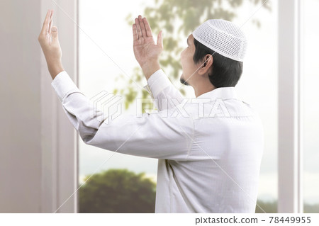 Rear view of Asian Muslim man sitting while raised hands and praying Rear view of Asian Muslim man sitting while raised hands and praying 78449955