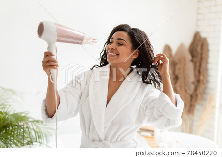 Happy Black Woman Drying Curly Hair With Hairdryer In Bathroom Happy Black Woman Drying Curly Hair With Hairdryer In Bathroom 78450220