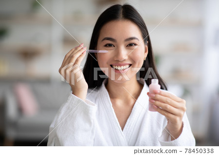 Pretty asian lady applying eye serum and smiling 78450338