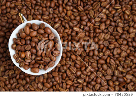 A white cup is peppered with beans against the background of coffee beans. Copy space. Top view. A white cup is peppered with beans against the background of coffee beans. Copy space. Top view. 78450589