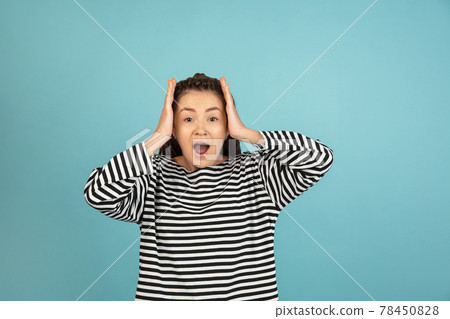 Wow. Beautiful female half-length front portrait isolated on blue studio backgroud. Young emotional surprised woman standing with open mouth. Human emotions, facial expression concept. 78450828