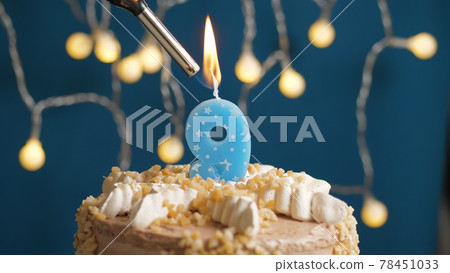 Birthday cake with 9 number candle on blue backgraund set on fire by lighter. Close-up Birthday cake with 9 number candle on blue backgraund set on fire by lighter. Close-up 78451033
