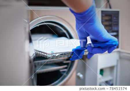 Dentist loading steel dental instruments sealed in separate airtight packaging in a steam autoclave for sterilization 78451574