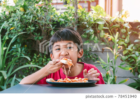 Asian cute boy in red shirt happily sitting eating pizza. 78451940