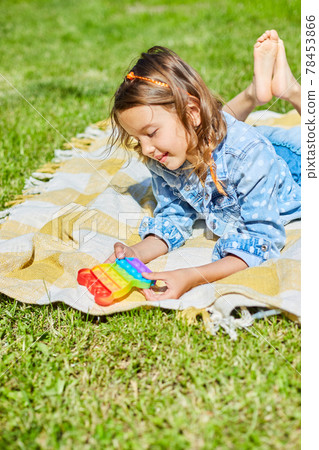 Girl lies on a blanket outdoors and play pop it, kid hands playing with colorful pop It Girl lies on a blanket outdoors and play pop it, kid hands playing with colorful pop It 78453866