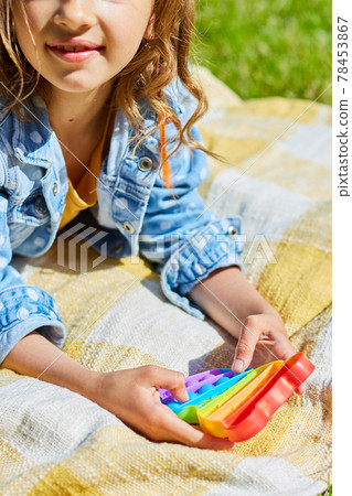 Girl lies on a blanket outdoors and play pop it, kid hands playing with colorful pop It Girl lies on a blanket outdoors and play pop it, kid hands playing with colorful pop It 78453867