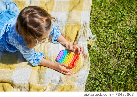 Girl lies on a blanket outdoors and play pop it, kid hands playing with colorful pop It Girl lies on a blanket outdoors and play pop it, kid hands playing with colorful pop It 78453868