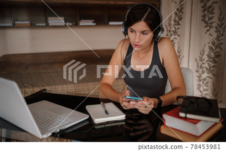 Shot of pretty young woman using her mobile phone while working with laptop sitting at home. Shot of pretty young woman using her mobile phone while working with laptop sitting at home. 78453981