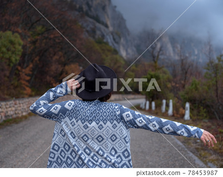 Stylish hipster woman in a hat walking down a mountain road Stylish hipster woman in a hat walking down a mountain road 78453987