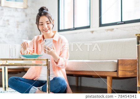 一位年輕女子在客廳吃意大利面時看著她的智能手機 78454341