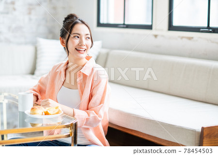 Young woman eating coffee and danish pastry for breakfast in the living room Young woman eating coffee and danish pastry for breakfast in the living room 78454503