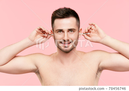 Young smiling man cleaning ears with cotton swab over pink background 78456746