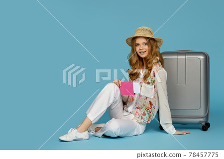 Happy blonde curly woman in hat sitting near suitcase 78457775