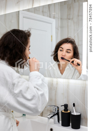 woman in white bathrobes brushing teeth in front of mirror woman in white bathrobes brushing teeth in front of mirror 78457894