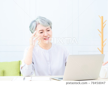 Senior asian woman holding head with hands while sitting and working with a laptop indoors. Senior asian woman holding head with hands while sitting and working with a laptop indoors. 78458047
