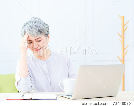 Senior asian woman holding head with hands while sitting and working with a laptop indoors. Senior asian woman holding head with hands while sitting and working with a laptop indoors. 78458050