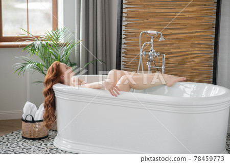 Beautiful ginger woman lying in a bath and looking pleased Beautiful ginger woman lying in a bath and looking pleased 78459773