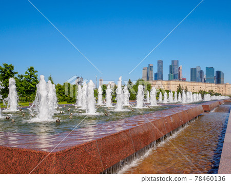Jets of fountains against the backdrop of skyscrapers and a cloudless blue sky. 78460136