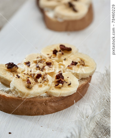 Sandwich with banana slices sprinkled with nuts close up on white wooden table. Sandwich with banana slices sprinkled with nuts close up on white wooden table. 78460229