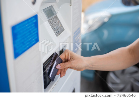 A woman fills her car with gasoline at a self-service gas station and pays with a credit card at a machine 78460546