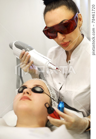 Woman treating client face with laser 78461720
