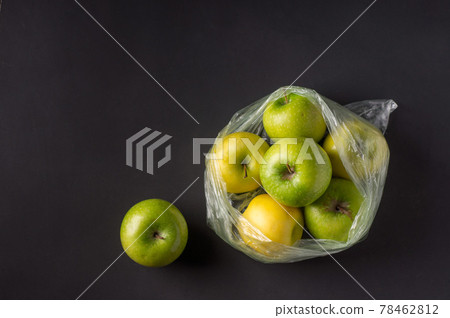 single use plastic packaging issue. green apples in plastic bags  on a dark background 78462812