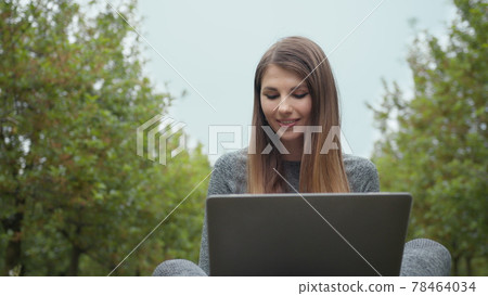 Woman opening laptop computer and starting to type on keyboard, trees at nature. Women engaging in business or freelance at nature or fresh air at amazing sun light. Girl sitting in park or forest 78464034