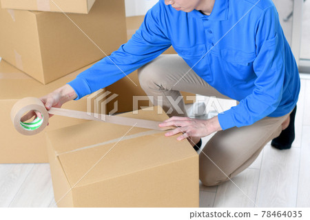 Image of a man wearing work clothes packing a moving cardboard 78464035