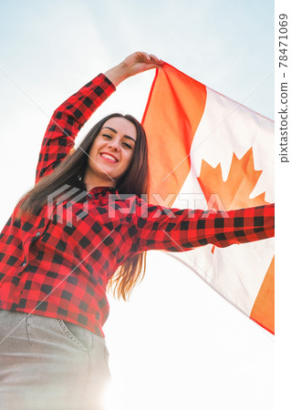 Young millennial brunette woman holding The National Flag of Canada. Canadian Flag or the Maple Leaf. Tourist traveler or patriotism. Immigrant in a free country. Independence day 1th july Young millennial brunette woman holding The National Flag of Canada. Canadian Flag or the Maple Leaf. Tourist traveler or patriotism. Immigrant in a free country. Independence day 1th july 78471069