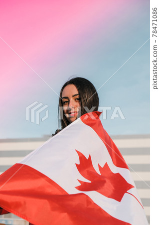 Young millennial brunette woman holding The National Flag of Canada. Canadian Flag or the Maple Leaf. Tourist traveler or patriotism. Immigrant in a free country. Independence day 1th july 78471086