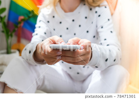 Young millennial hippie woman sitting on balcony using mobile phone. LGBTQ rainbow flag on background. Phone texting, video call, taking selfie. Blogger. Work from home. Young millennial hippie woman sitting on balcony using mobile phone. LGBTQ rainbow flag on background. Phone texting, video call, taking selfie. Blogger. Work from home. 78471301