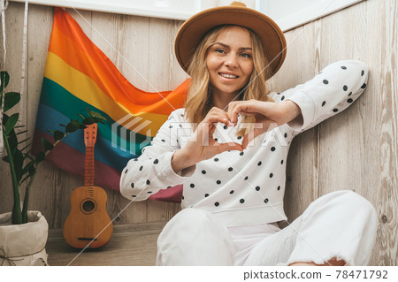 Young blonde millennial hippie woman with rainbow LGBTQ flag at home balcony. Peace and freedom the symbol of LGBT, spending and sharing loving time. Support LGBTQ community. Young blonde millennial hippie woman with rainbow LGBTQ flag at home balcony. Peace and freedom the symbol of LGBT, spending and sharing loving time. Support LGBTQ community. 78471792